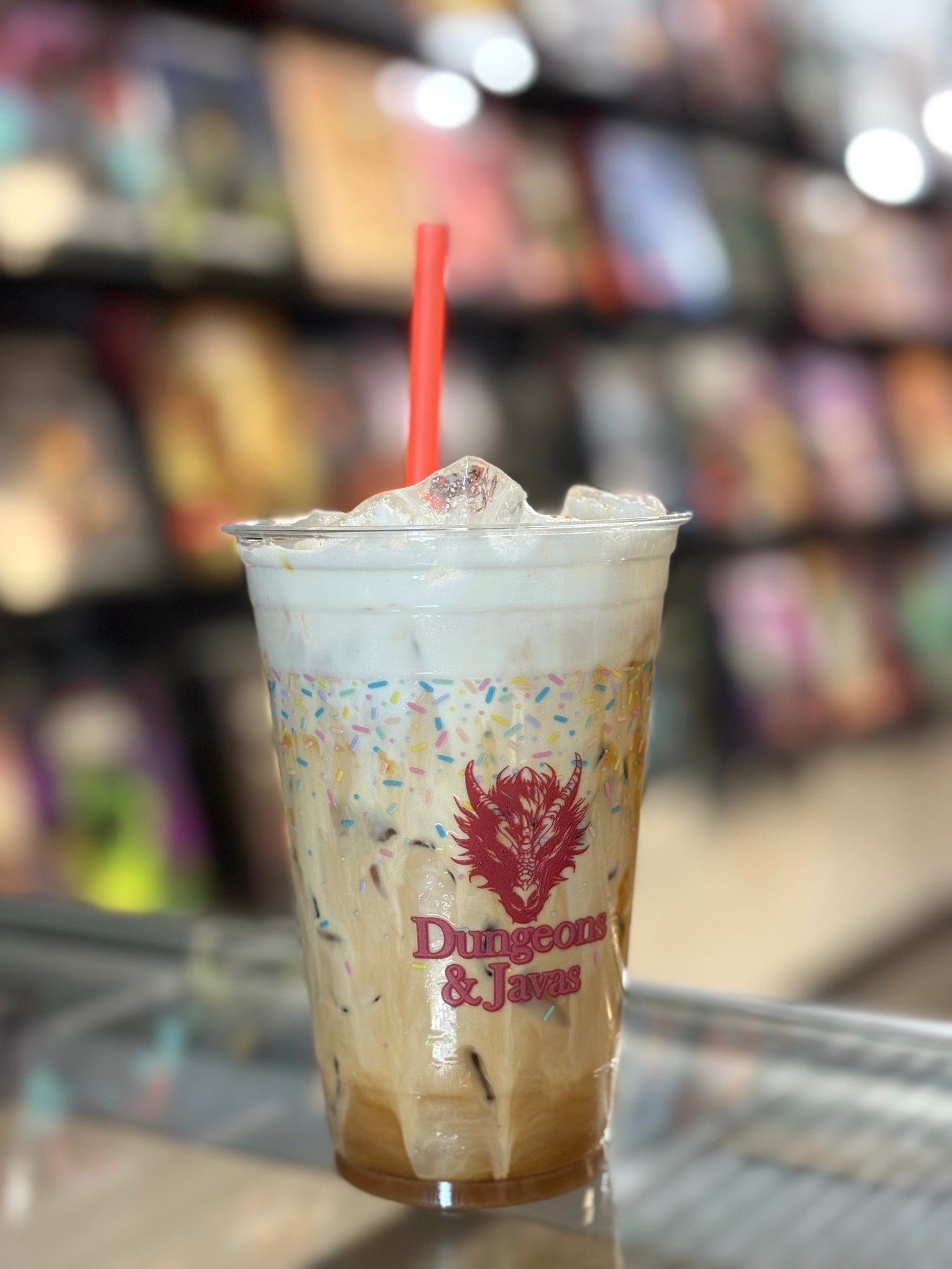 Frappuccino with a red straw in a cup featuring 'Dungeons & Dragons' logo, against a blurred bookshelf background.