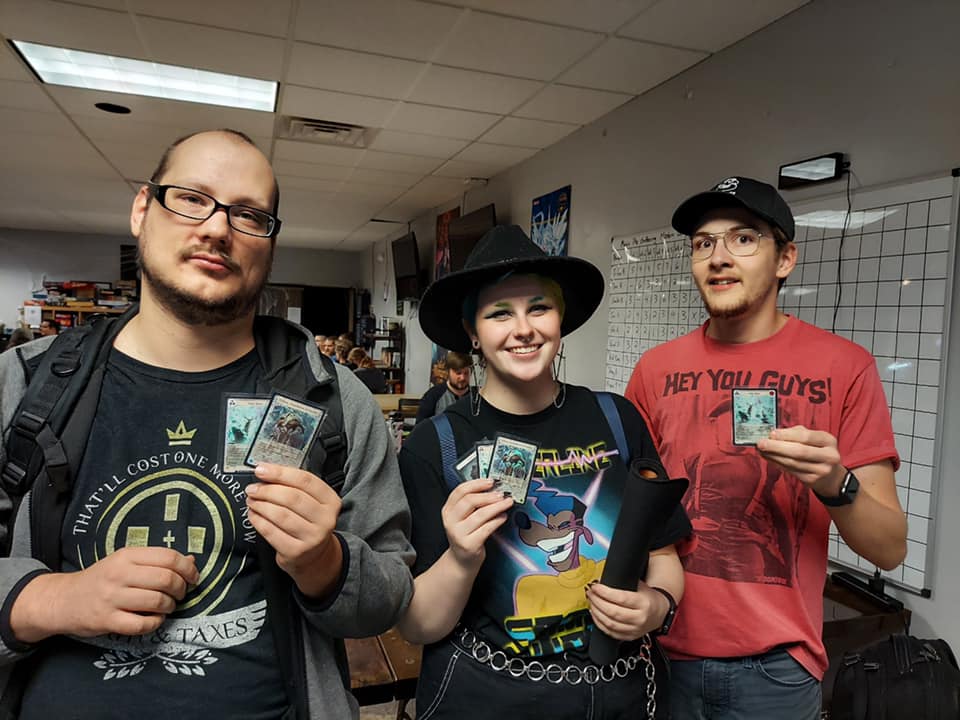 Three people holding trading cards in a game shop setting