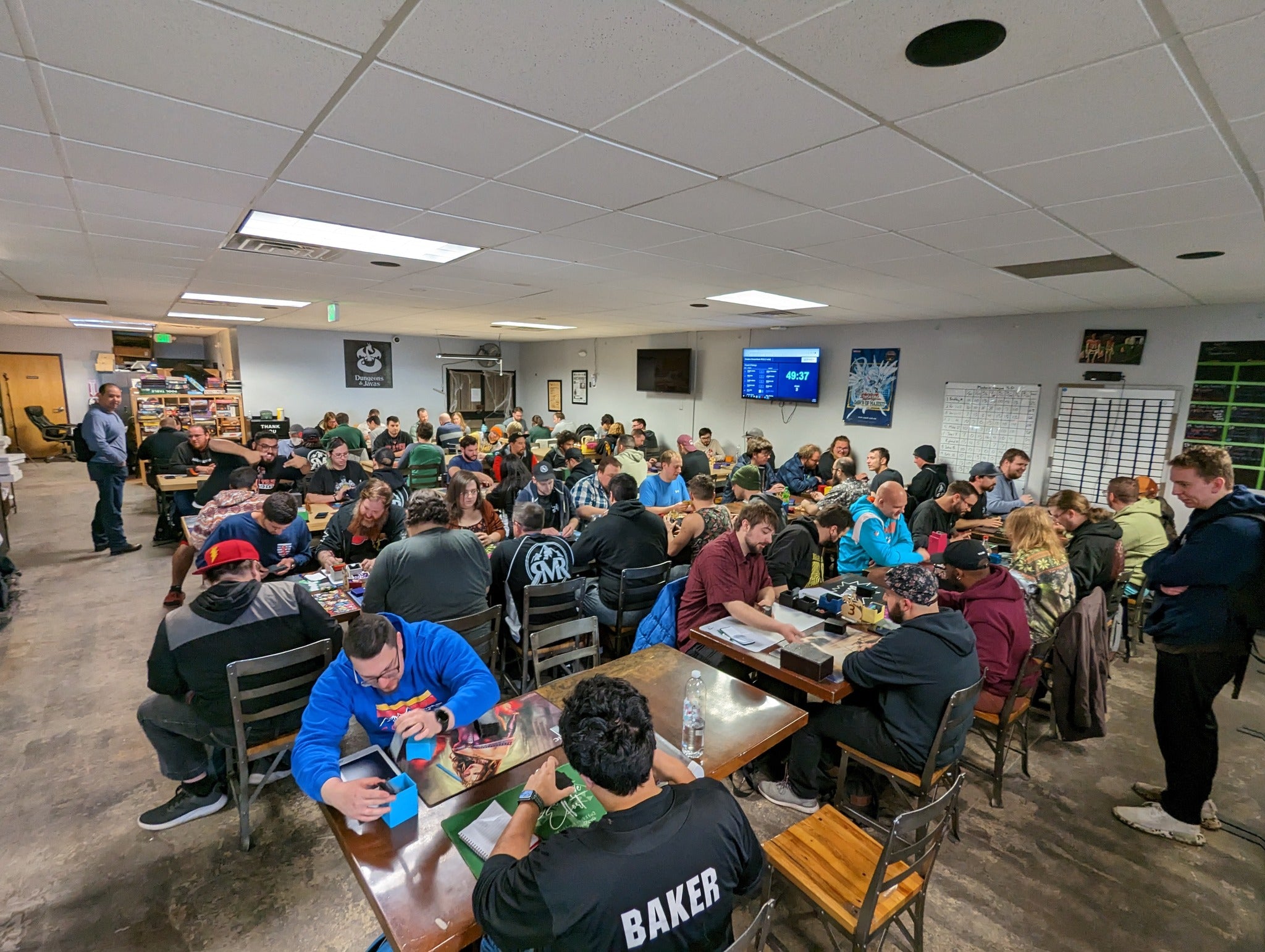Group of people sitting at tables in a large room, participating in game event in Colorado Springs at Dungeons & Javas.