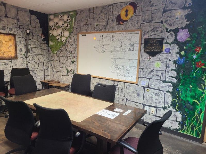 Room with a table and chairs against a wall with decorative maps and drawings.