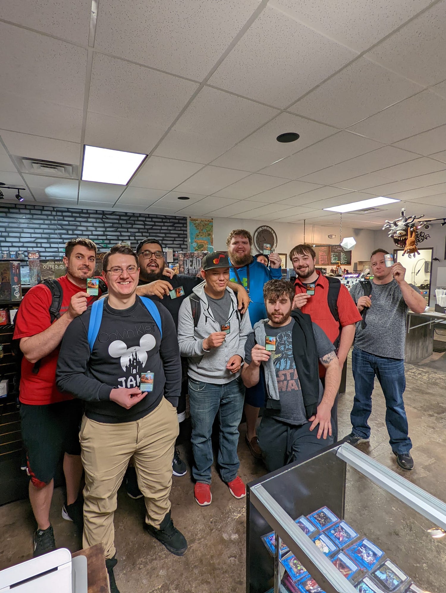 Group of people posing together in a game store with a display case in the foreground.